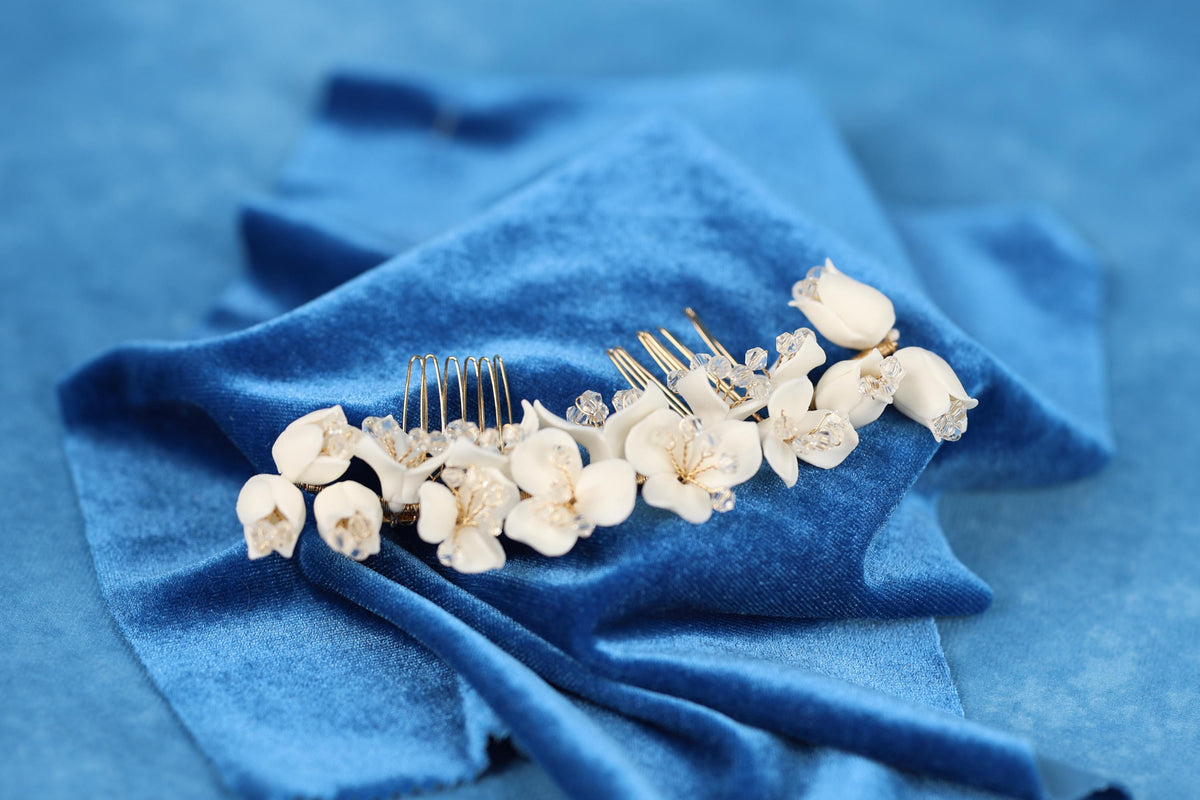 A close-up view of a decorative hair accessory, possibly a hair clip or headband, adorned with small white flowers or buds, resting on a blue fabric surface.