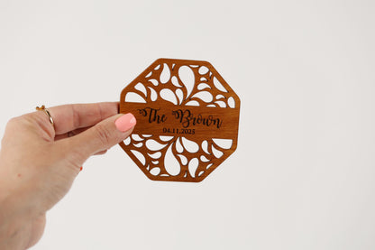 A hand holding a wooden coaster with the text "The Brown" and the date "04.11.2025" printed on it.