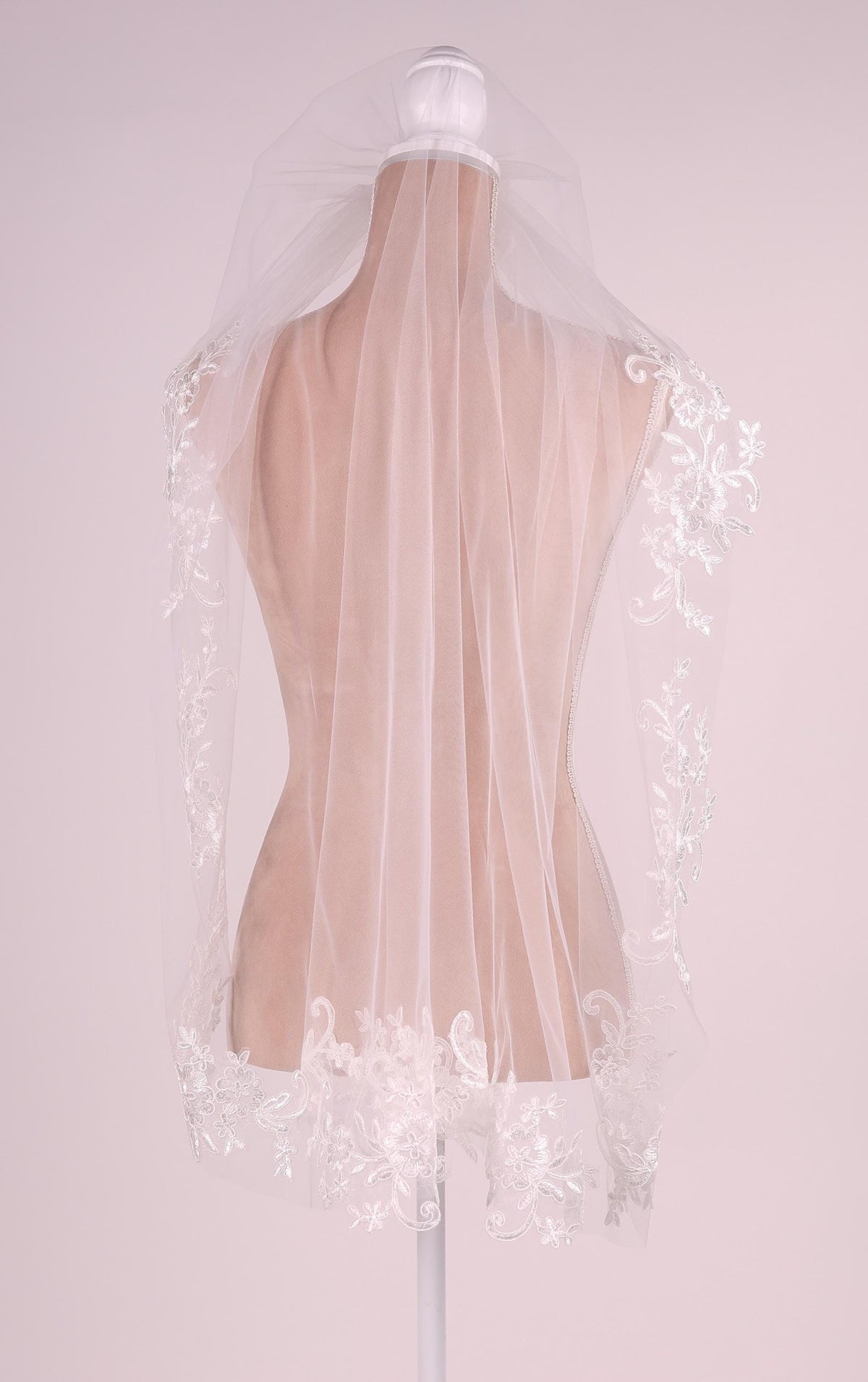 A mannequin wearing a white veil with delicate floral embroidery.