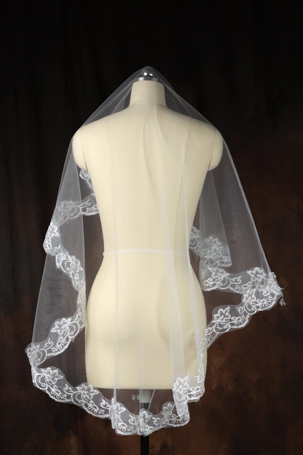 A white mannequin wearing a white veil with a delicate lace trim.