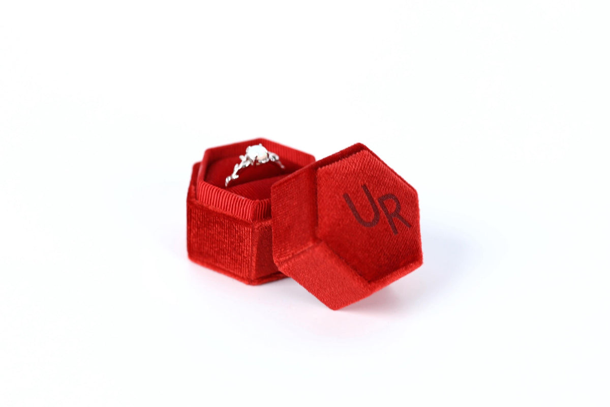 A red velvet box containing a diamond ring, with the word "UR" visible on the side of the box.