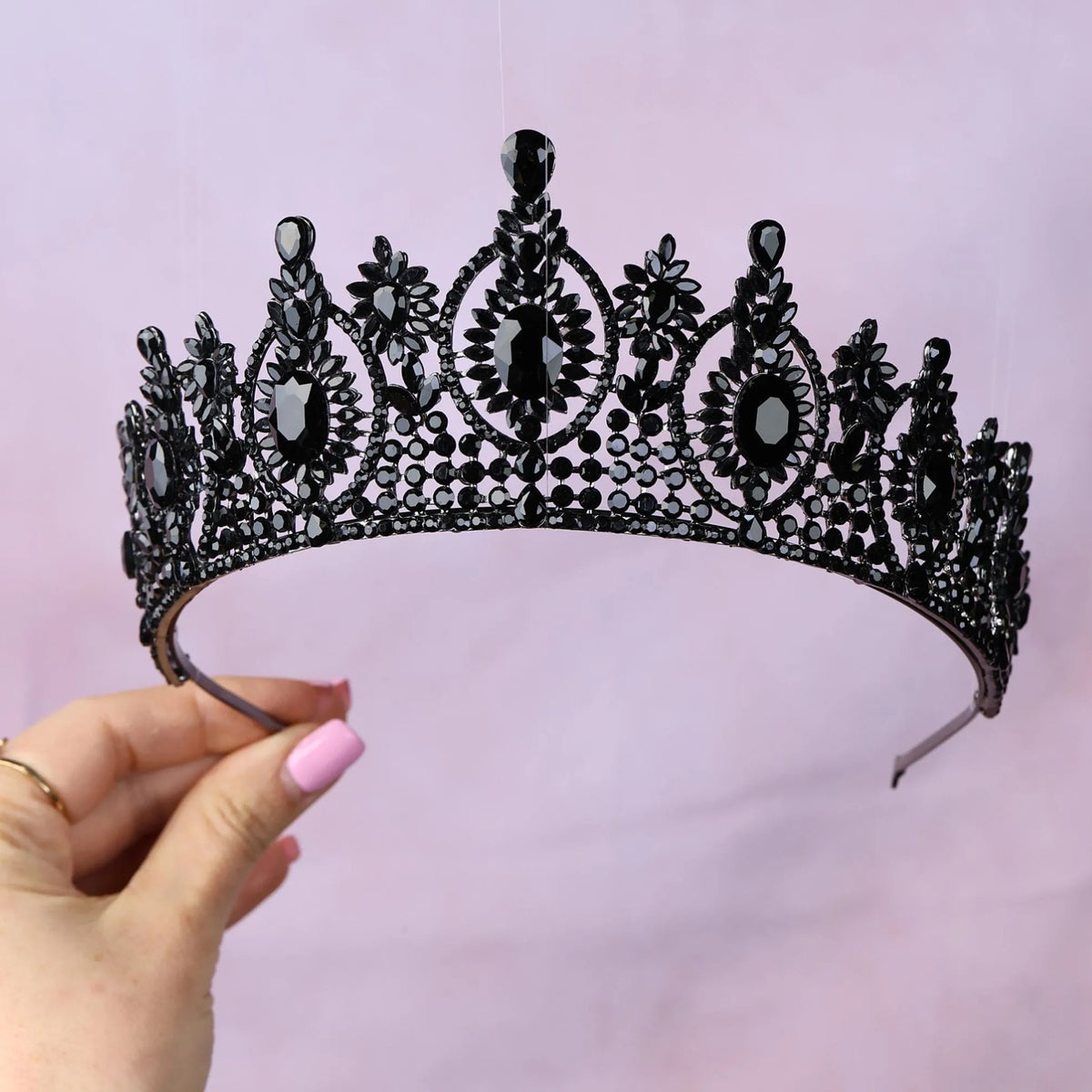 a hand holding a black tiara against a pink background