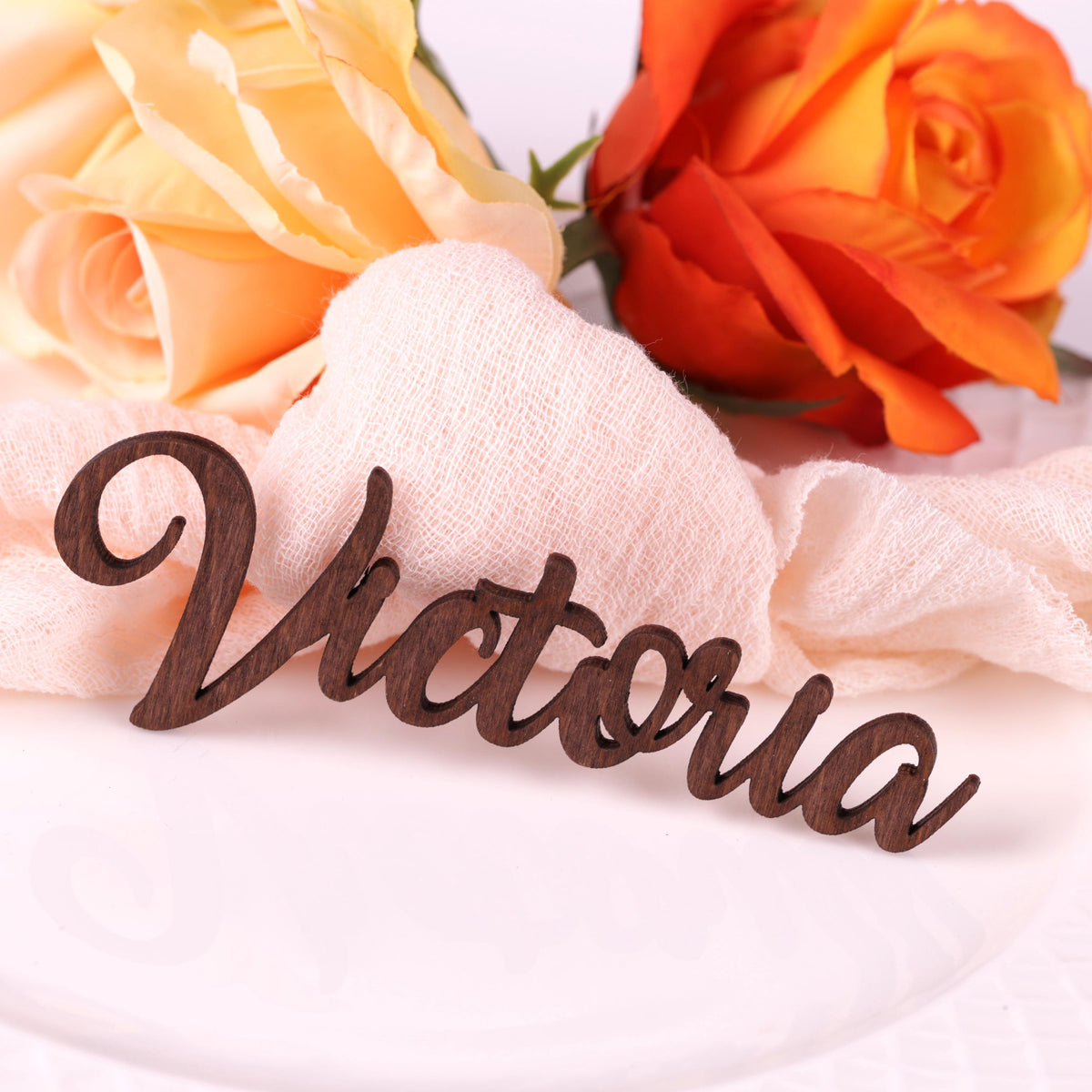 a wooden nameplate with the name "Victoria" written on it, placed on a white surface next to two roses.