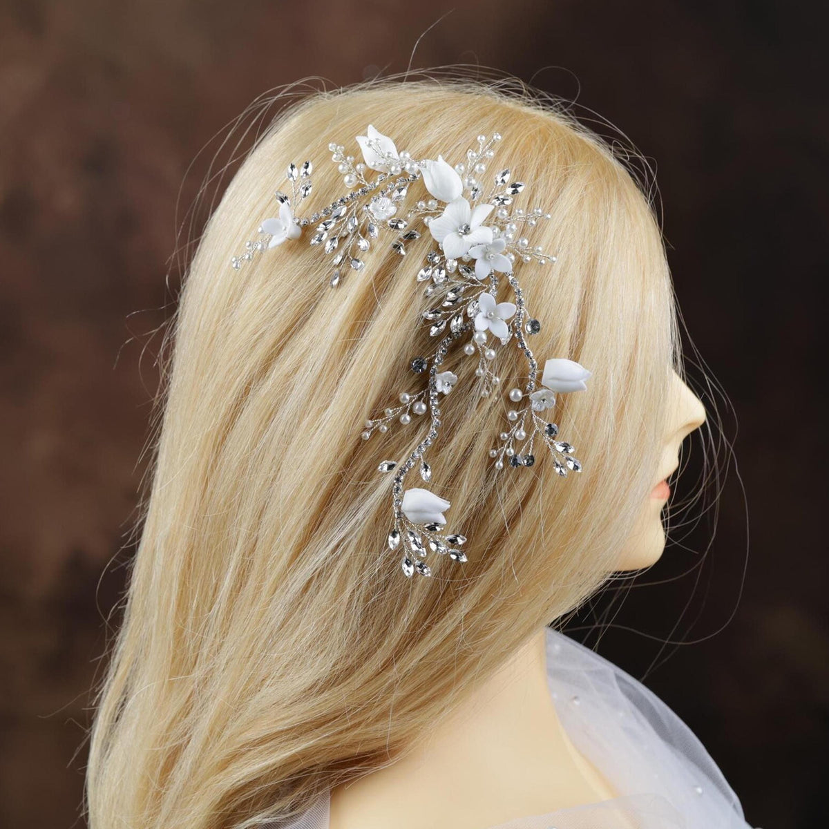 A mannequin head with blonde hair styled in a side profile, adorned with a decorative hair accessory featuring white flowers and crystals.