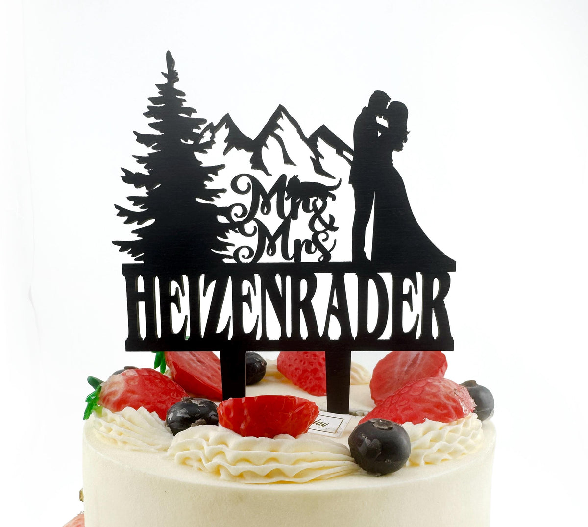 A black silhouette of a couple embracing on top of a cake, with the word "HEIZENRADER" written on the cake topper.