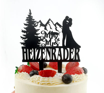 A black silhouette of a couple embracing on top of a cake, with the word "HEIZENRADER" written on the cake topper.