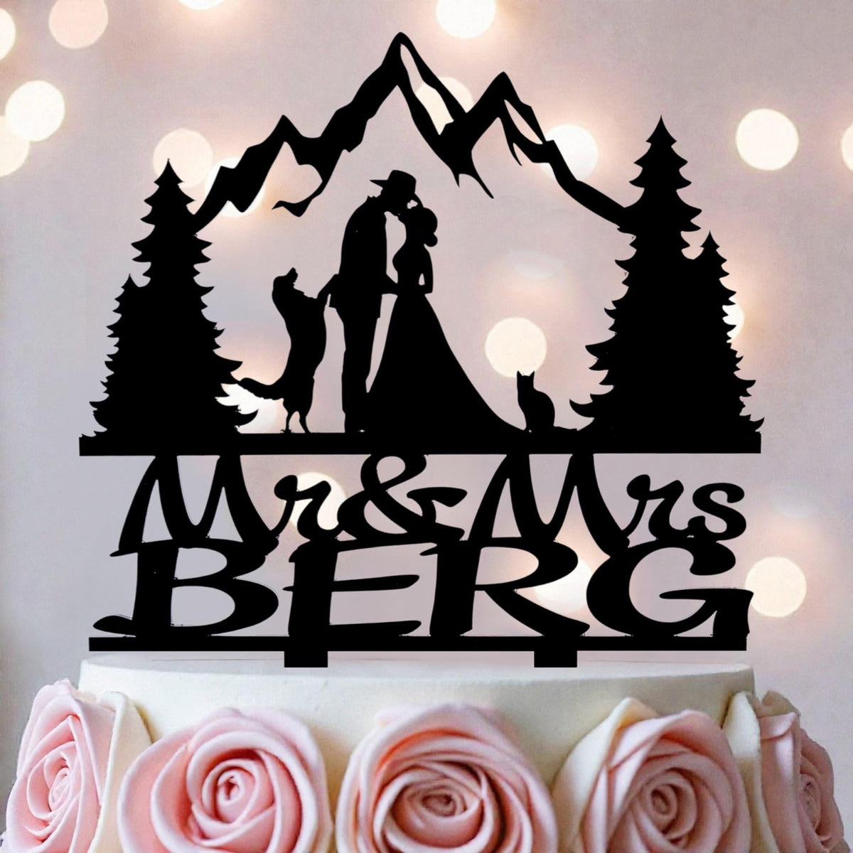 A silhouette of a couple embracing, with a mountain landscape in the background, is depicted on a cake topper.
