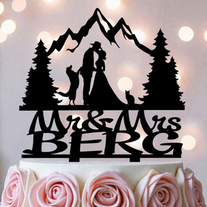 A silhouette of a couple embracing, with a mountain landscape in the background, is depicted on a cake topper.