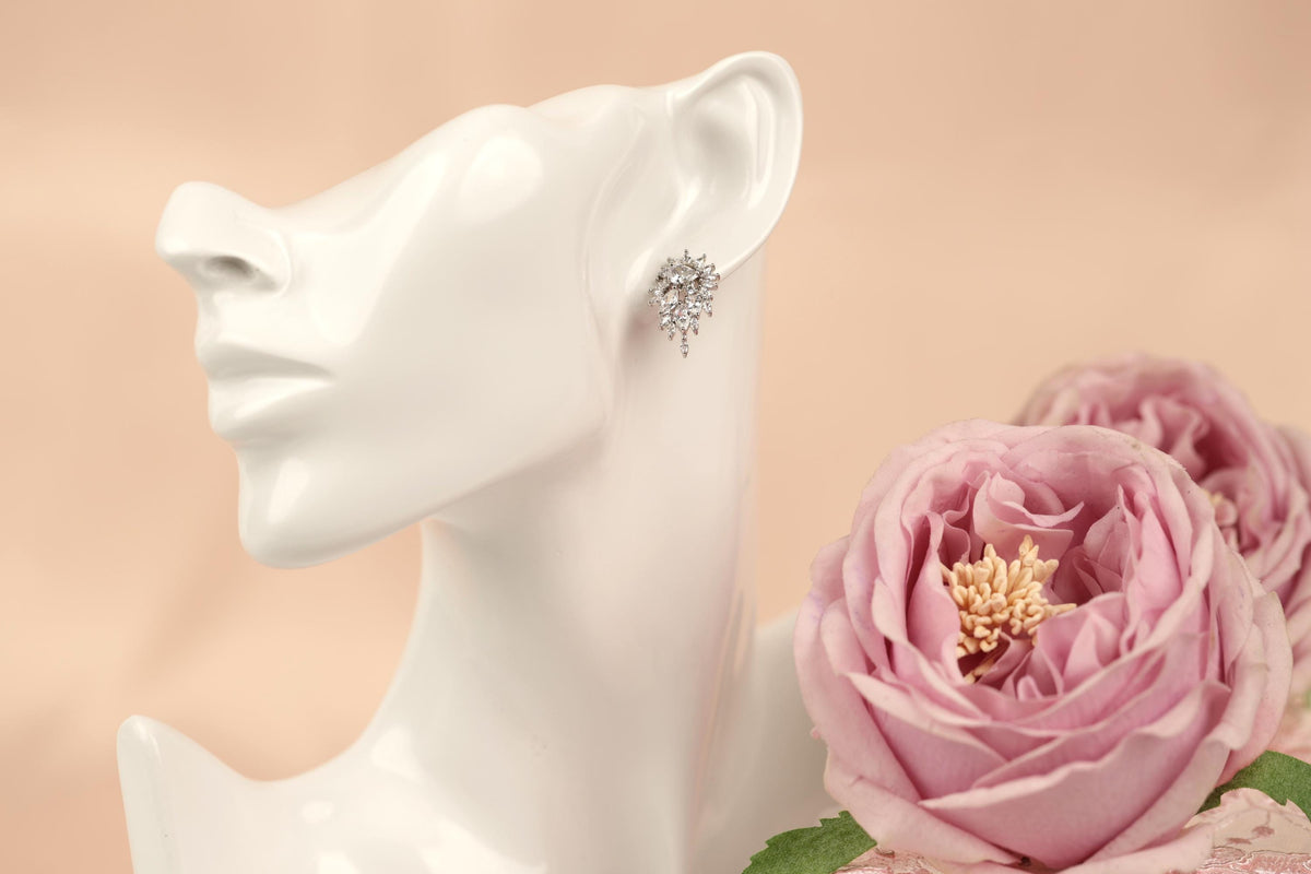 A white mannequin head wearing a pair of earrings with a floral design, accompanied by a bouquet of pink roses.