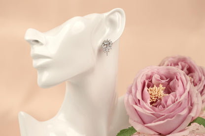 A white mannequin head wearing a pair of earrings with a floral design, accompanied by a bouquet of pink roses.