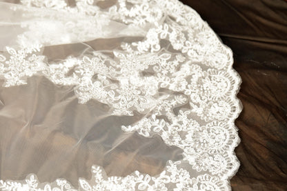 A close-up view of a delicate, white lace veil with intricate floral patterns.