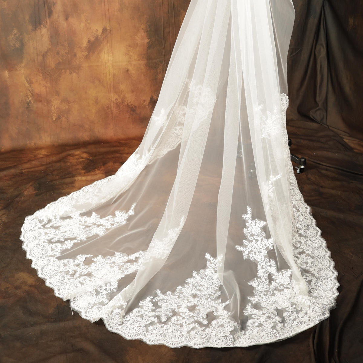 A close-up view of a white wedding veil with intricate lace detailing, displayed against a brown background.