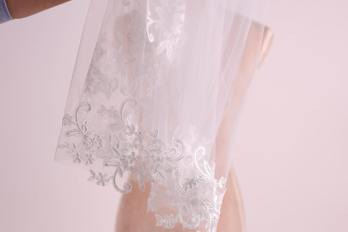 A close-up view of a delicate white wedding veil with intricate floral embroidery.