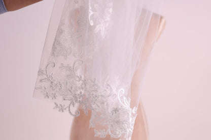 A close-up view of a delicate white wedding veil with intricate floral embroidery.