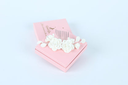 A pink box with a white comb and flowers on top, placed on a white background.