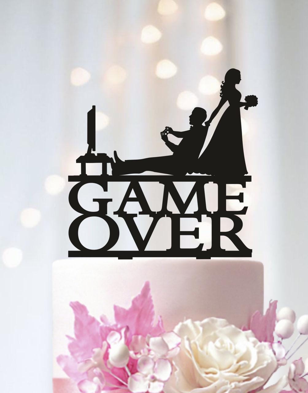 A black silhouette of a man and woman playing a video game on a cake topper, with the words "GAME OVER" written on it.