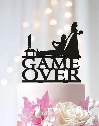 A black silhouette of a man and woman playing a video game on a cake topper, with the words "GAME OVER" written on it.