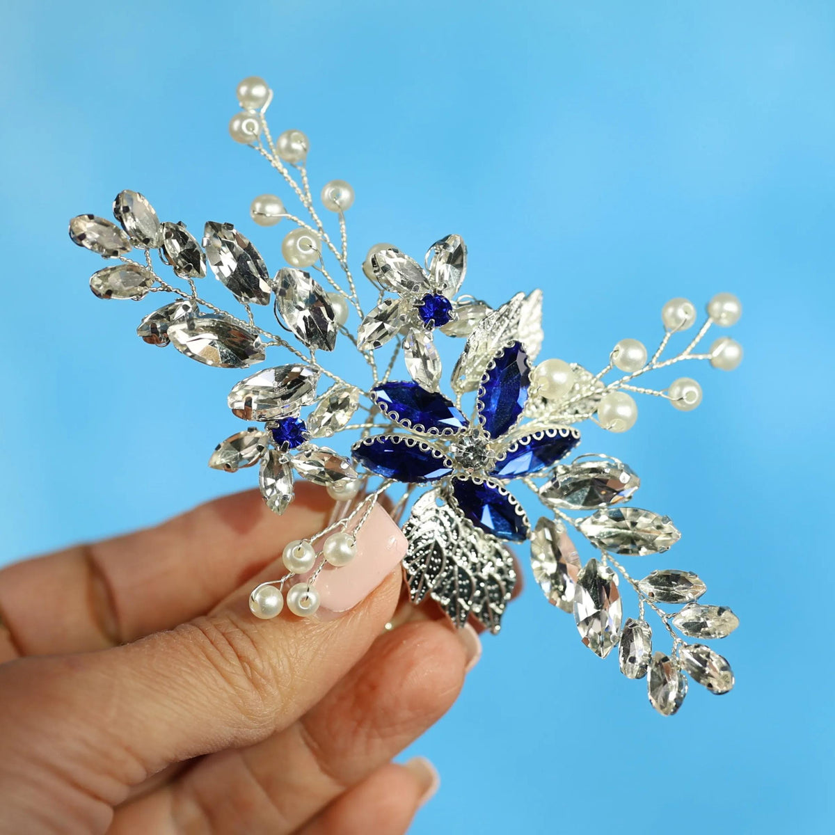 A hand holding a decorative piece of jewelry against a blue background.