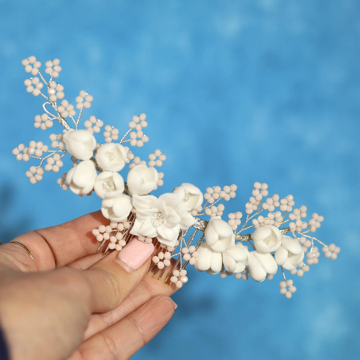 A hand holding a delicate floral hair accessory against a blue background.
