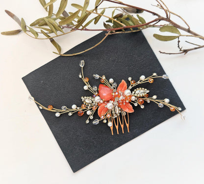 A decorative hair accessory with a floral design and sparkling embellishments, including a large red flower and numerous small pearls, is placed on a black surface alongside some green leaves.