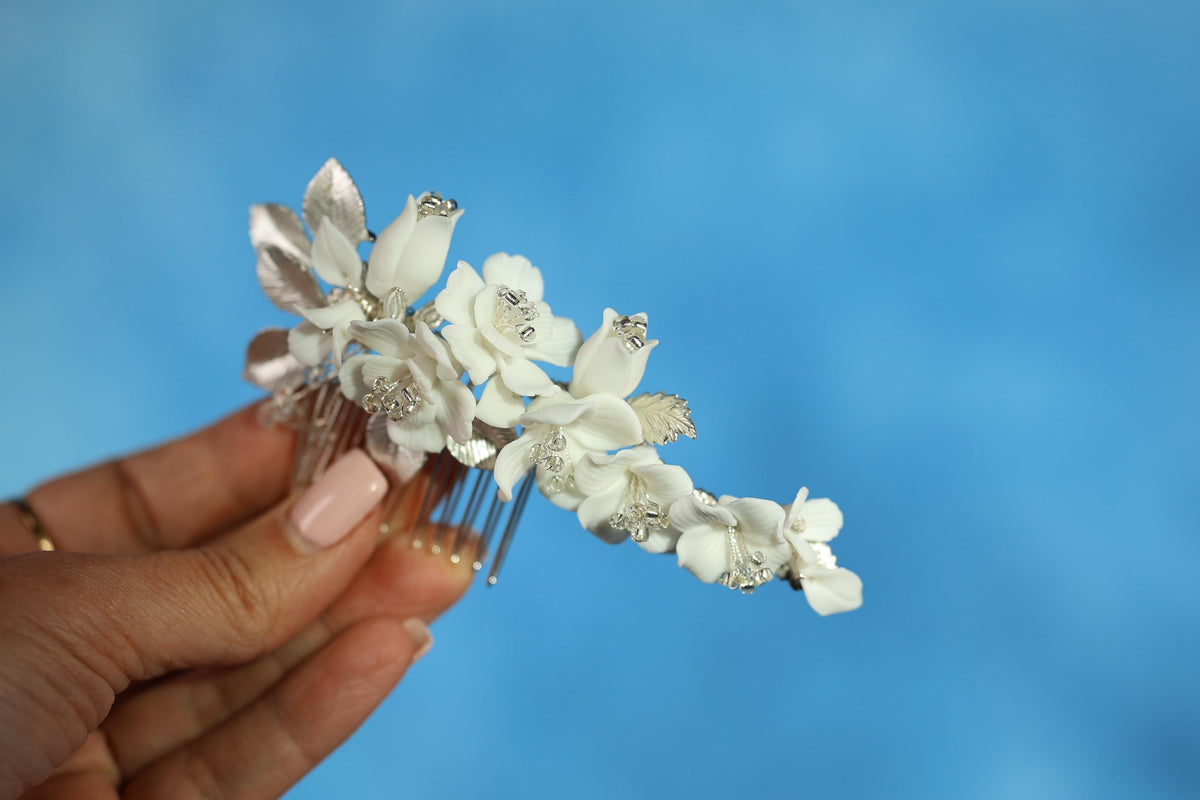 A hand holding a decorative hair accessory with white flowers against a blue background.