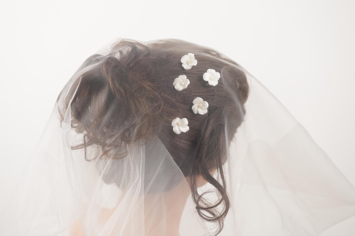 A close-up view of a person's head with a veil and white flower decorations on the hair.