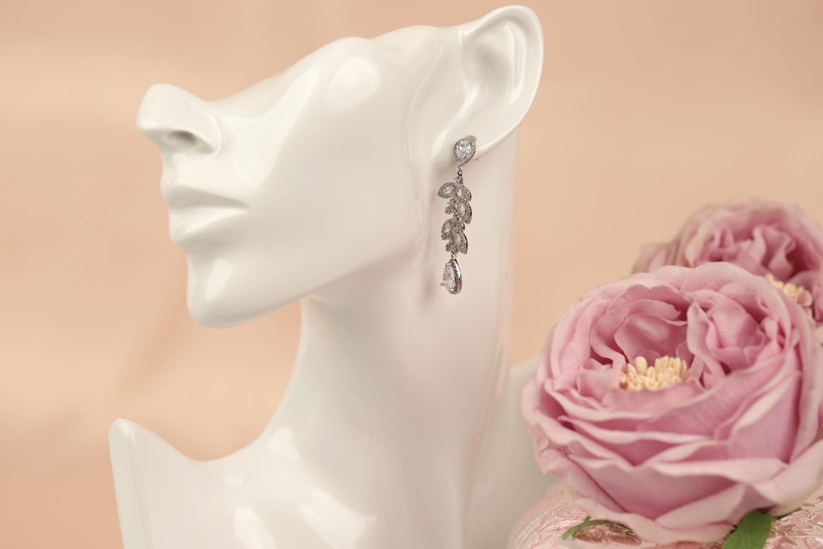 A white mannequin head wearing a pair of dangling earrings with a floral design, placed next to a bouquet of pink roses.