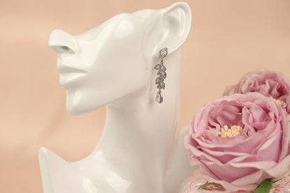 A white mannequin head wearing a pair of dangling earrings with a floral design, placed next to a bouquet of pink roses.