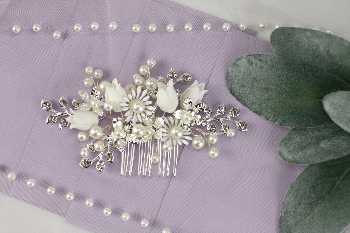 A decorative hair accessory with white flowers and pearls is displayed on a purple background, accompanied by a green leaf and a string of pearls.