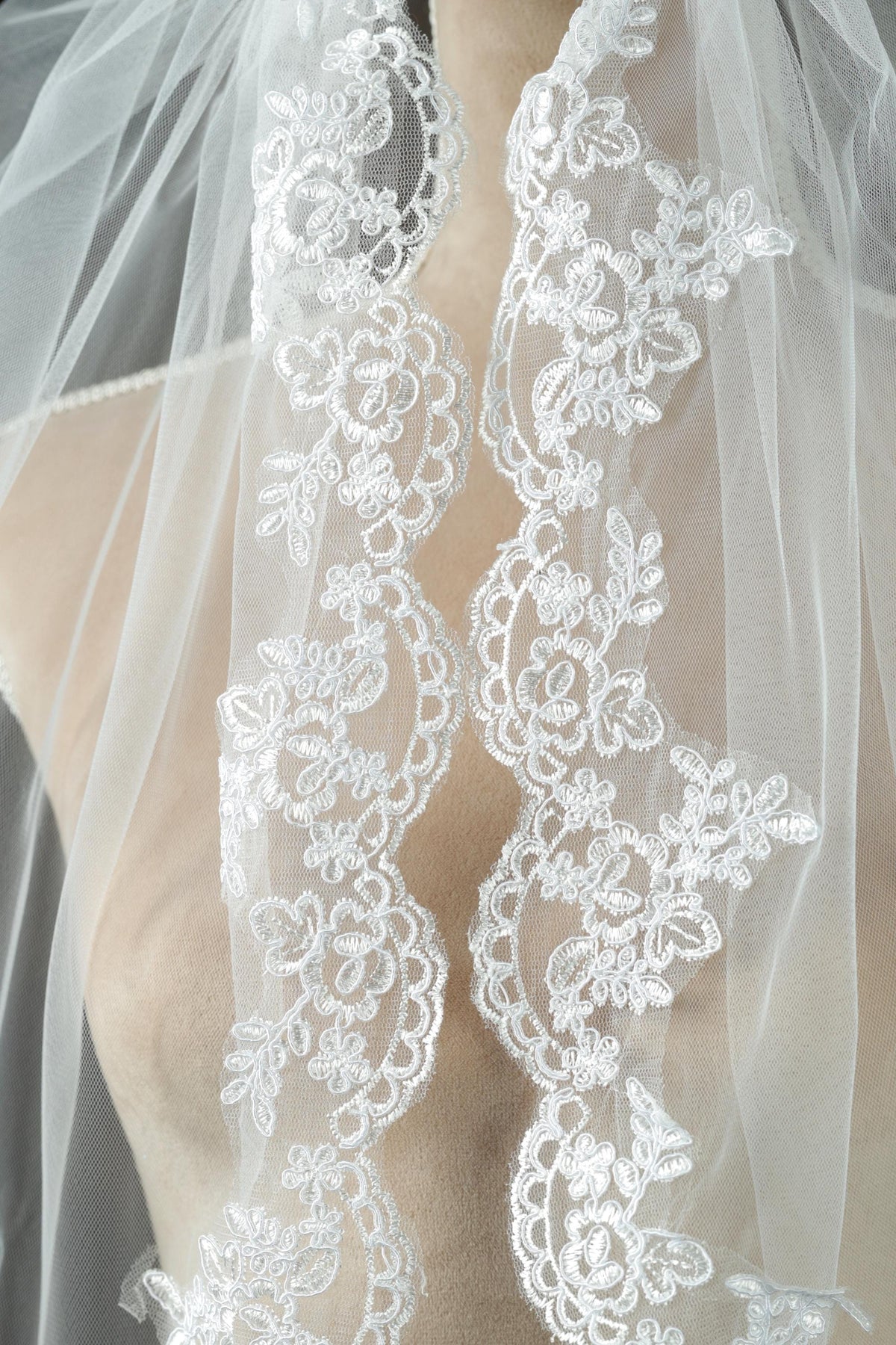A close-up view of a delicate white lace veil with intricate floral embroidery.