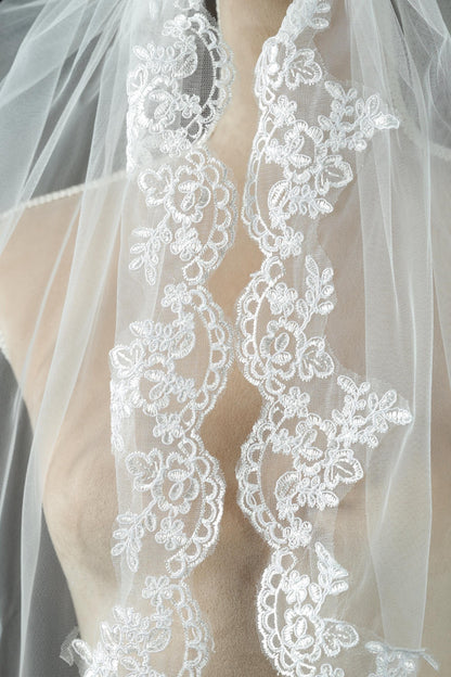 A close-up view of a delicate white lace veil with intricate floral embroidery.