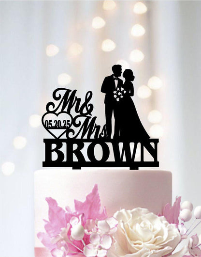 A black silhouette of a bride and groom on a wedding cake topper, with the text "Mr & Mrs Brown" and the date "05.20.25" displayed below.
