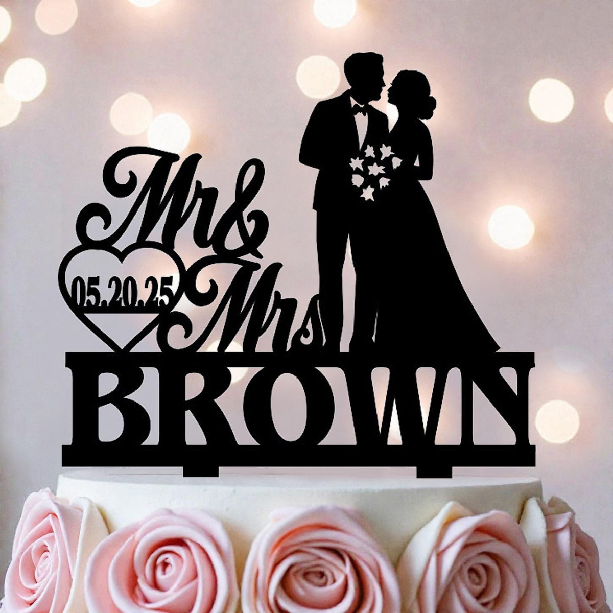 A black silhouette of a bride and groom on a wedding cake topper, with the text "Mr & Mrs BROWN" and the date "05.20.25" displayed.