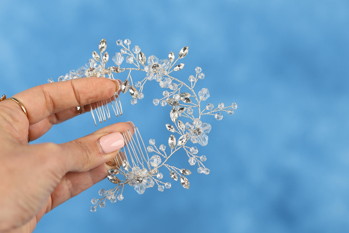 A hand holding a decorative hair accessory with clear crystal or gemstone embellishments against a blue background.