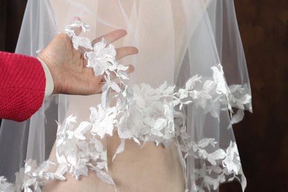 A hand is holding a delicate white lace veil with intricate floral patterns.