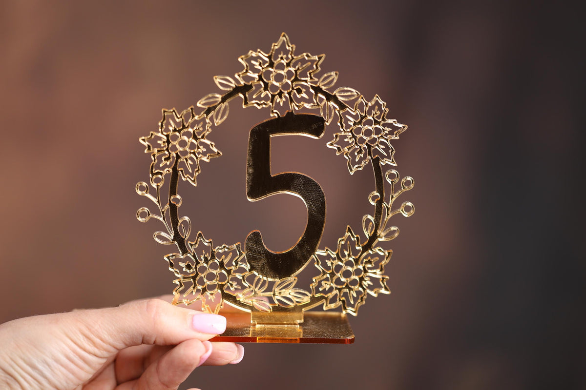 A hand holding a decorative gold-colored number 5 holder with a floral design.