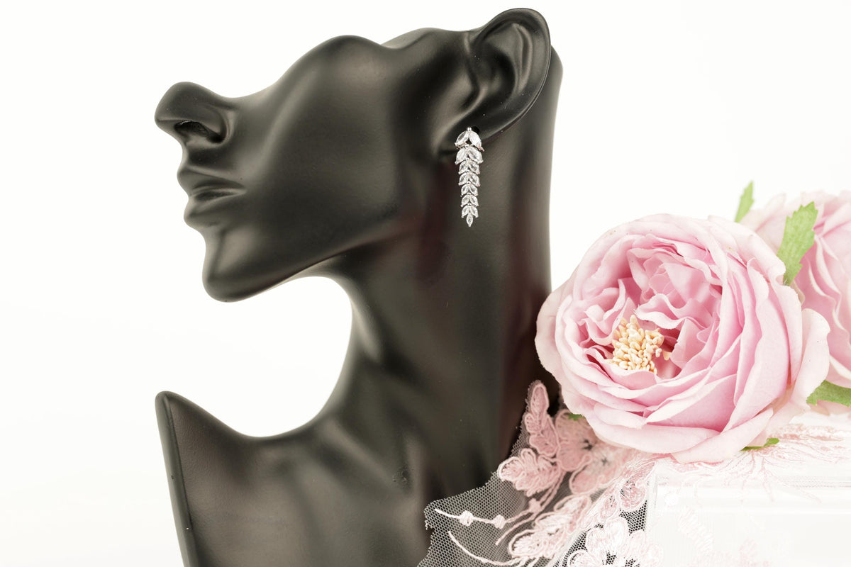 A black mannequin head wearing a pair of silver earrings with a delicate floral design, accompanied by a pink rose.