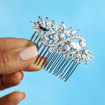 A hand holding a decorative hair accessory with a floral design against a blue background.