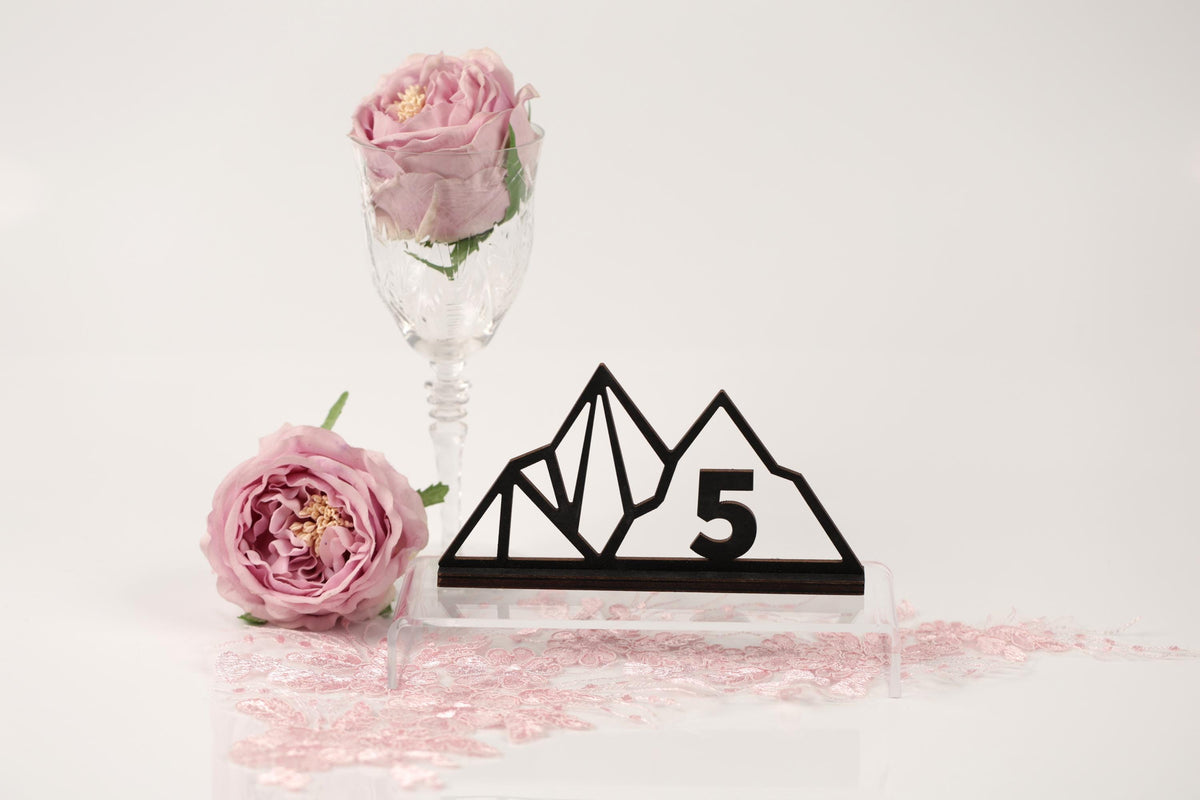 a pink rose, a glass vase, a black and white mountain-shaped object with the number 5, and pink glitter on a white background.