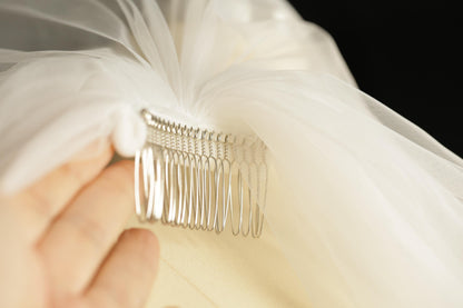 A hand holding a silver hair clip with a white veil attached to it.