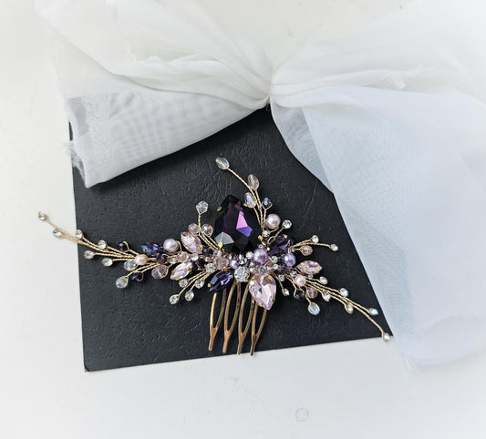 A decorative hair accessory with a gold-colored comb and a large purple gemstone, placed on a black surface.