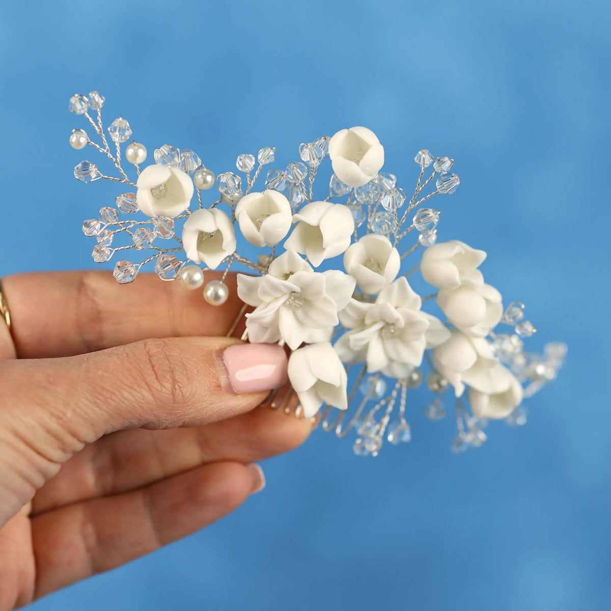 A hand holding a delicate white flower arrangement against a blue background.