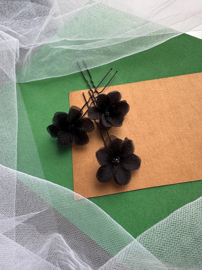 three black flower-shaped hair clips arranged on a green background.