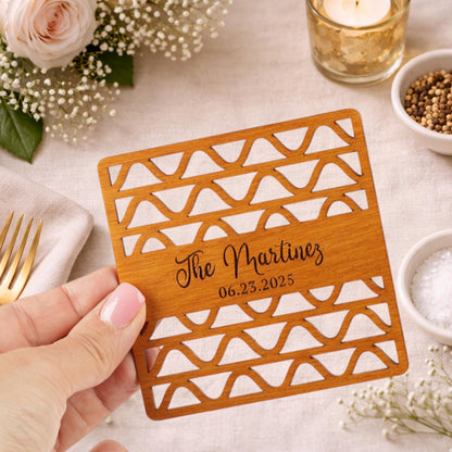 A hand holding a wooden coaster with text and a date printed on it, surrounded by other items such as a rose, a candle, and a bowl of spices.