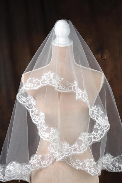 A white wedding veil with intricate lace detailing is displayed on a mannequin.