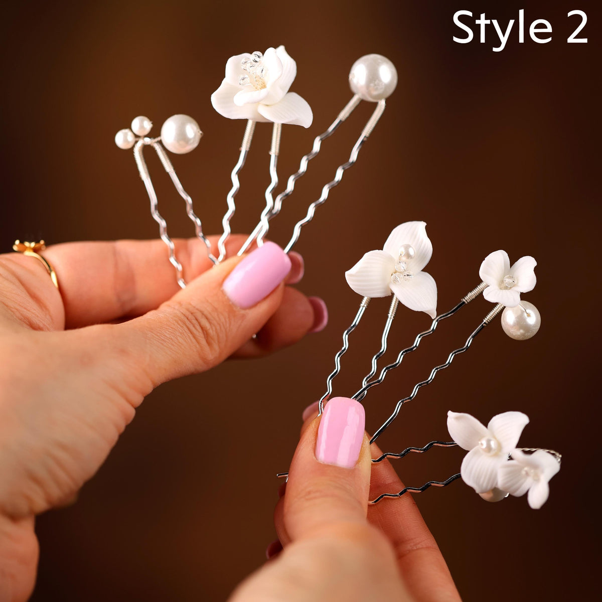 A close-up image of a person's hands holding several silver hair clips with white flower-shaped decorations on them.