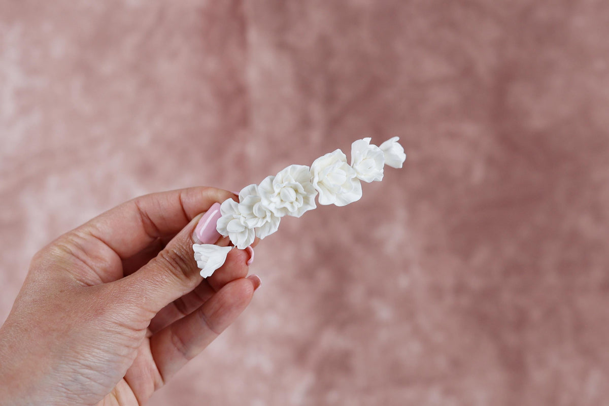 A hand holding a delicate flower accessory against a pink background.