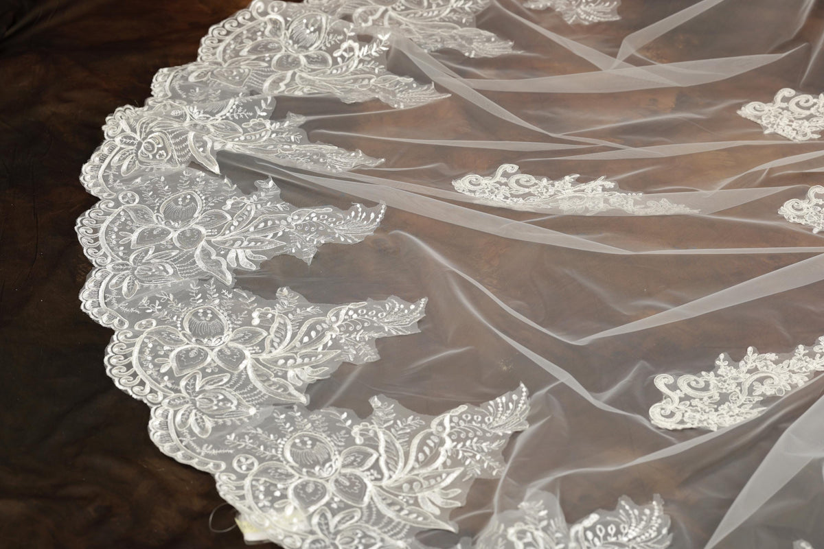 a close-up view of a delicate, white lace veil with intricate floral patterns. The veil appears to be made of sheer fabric, giving it a delicate and elegant appearance.