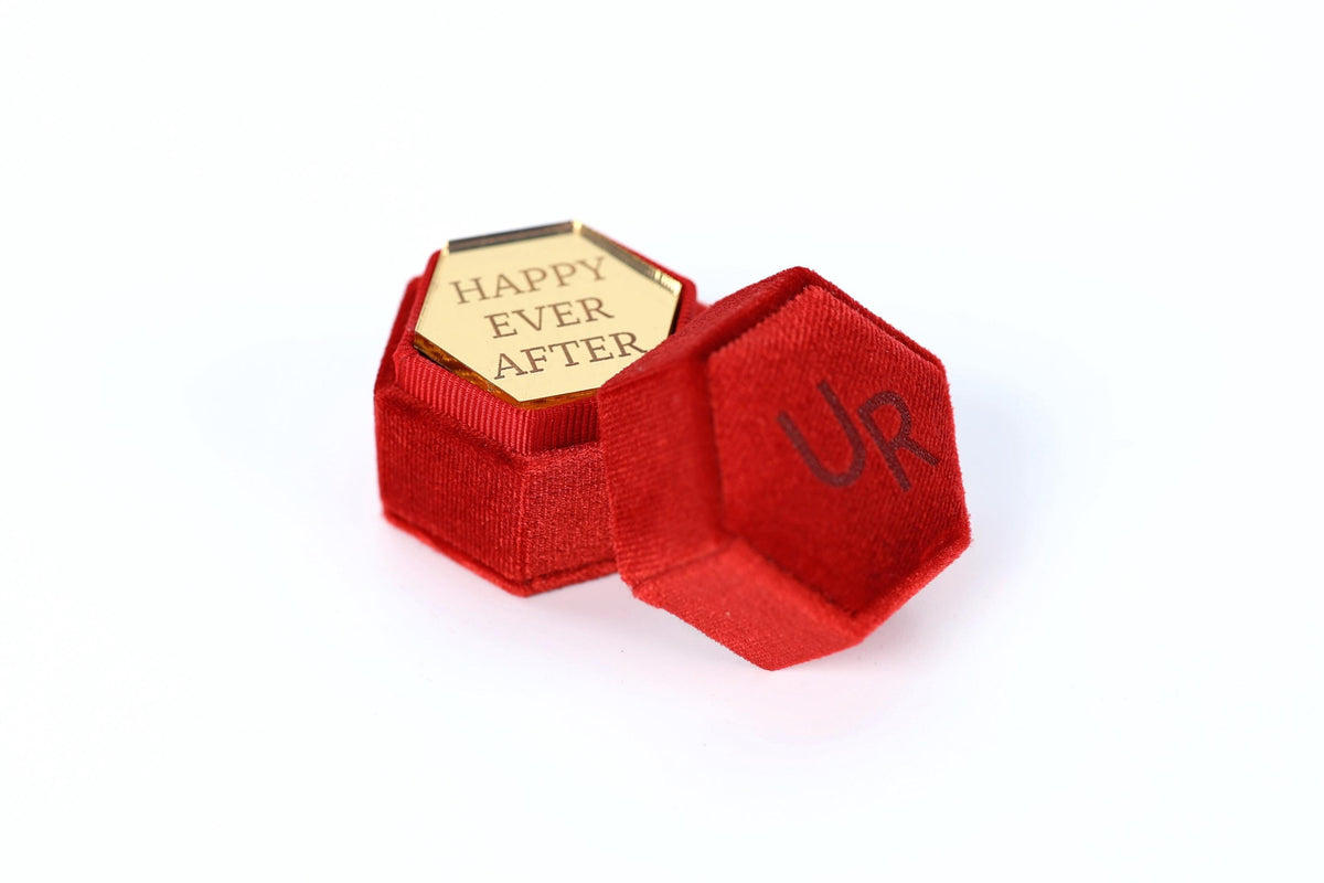 a red velvet box with a gold-colored hexagonal plaque inside. The plaque has the text "HAPPY EVER AFTER" engraved on it.