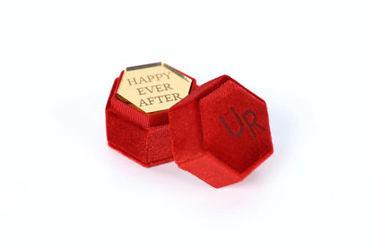 a red velvet box with a gold-colored hexagonal plaque inside. The plaque has the text "HAPPY EVER AFTER" engraved on it.